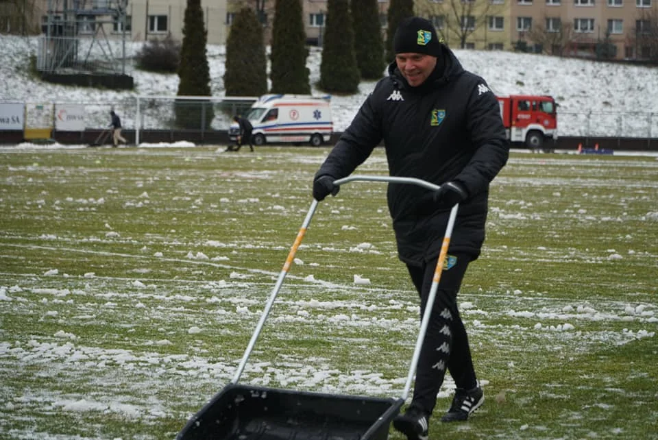 Piłkarze i sztab trenerski Siarki Tarnobrzeg odśnieżają murawę obiektu w Jastrzębiu